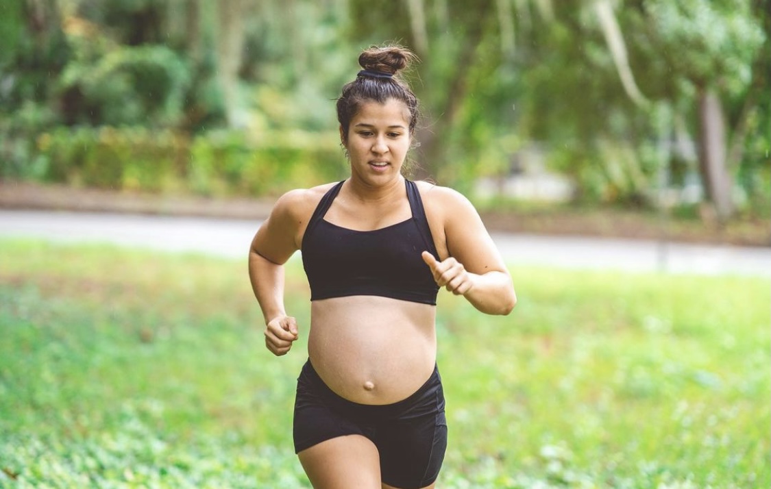 A pregnant woman running in a tank top and shorts.