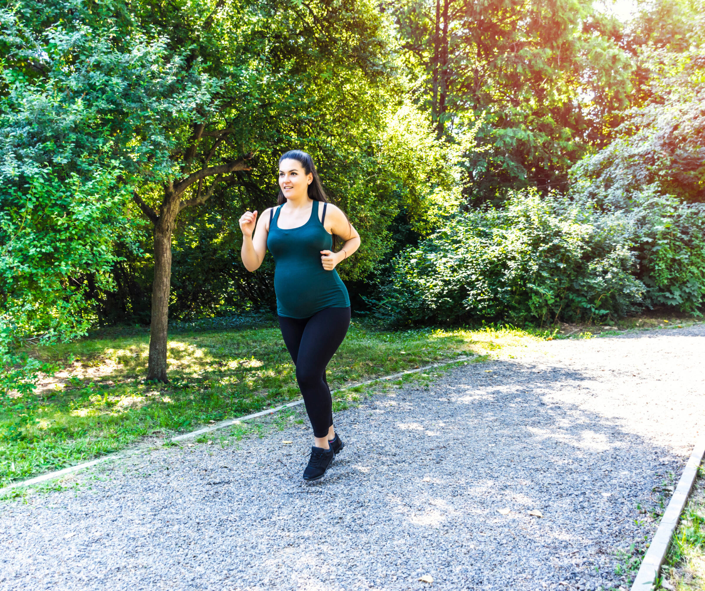 A pregnant woman running on a gravel trail. 