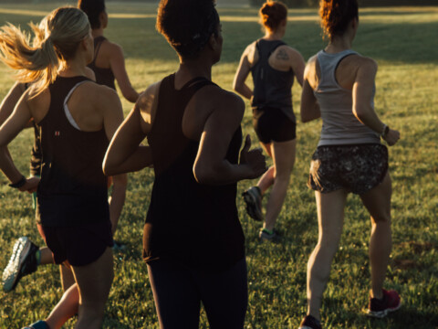 women running in a field at sunrise