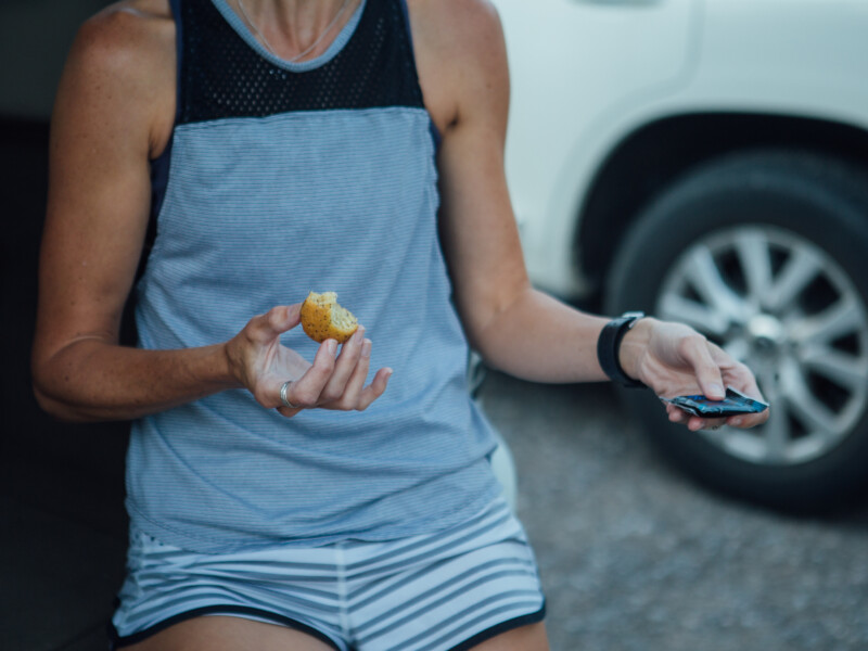 a woman eating a bagel on the tailgate of a ear