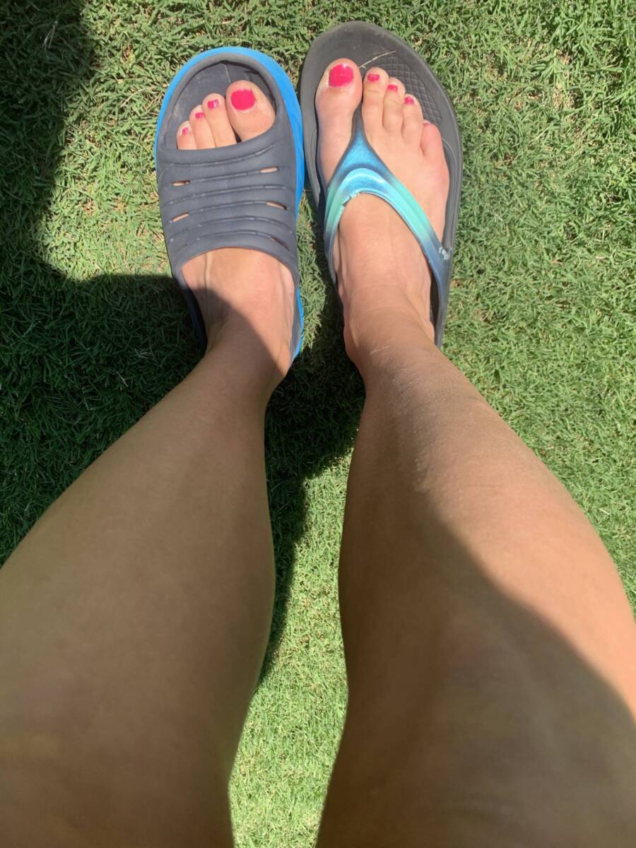Overhead shot of one foot in a OOFOs sandal and the other in a Hoka slide.