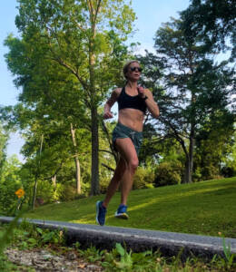 Woman running on a street in a black sports bra and green shorts.