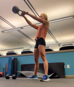 Whitney Heins doing a kettlebell swing in a pink shirt