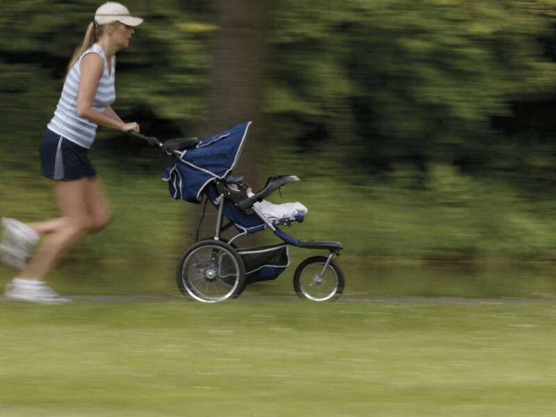 woman in hat running on grassy trail pushing a stroller.